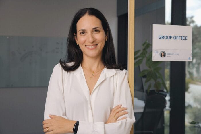 Maayan smiling with her arms folded and leaning against the door frame in her office.