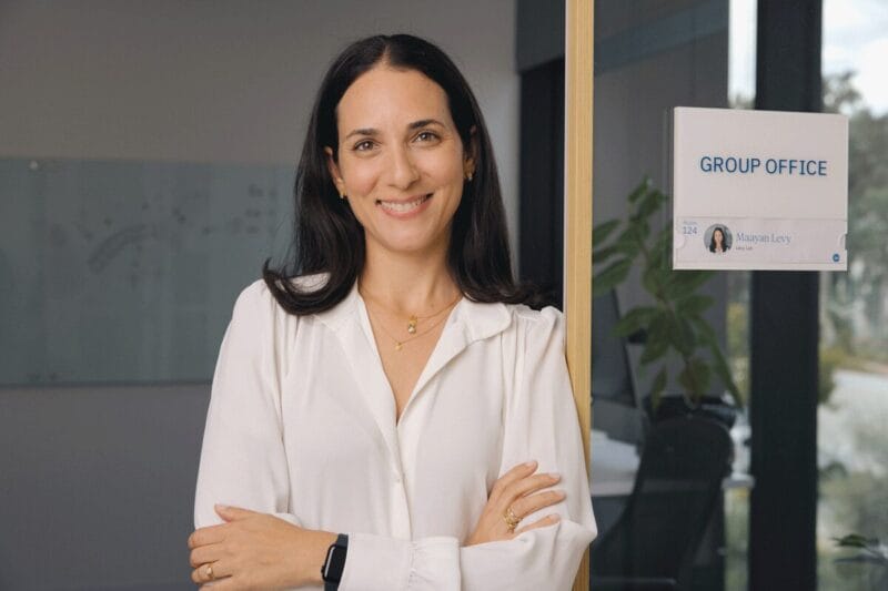 Maayan smiling with her arms folded and leaning against the door frame in her office.