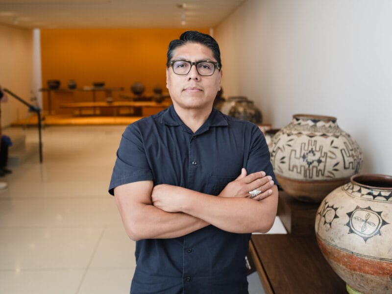 Brian Vallo, standing arms folded, in a pottery exhibition.