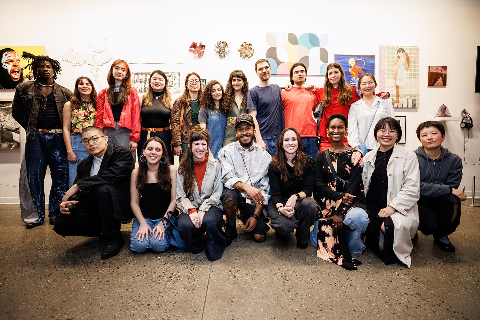 A group of young adults, some standing and some kneeling, pose for a photo in an art gallery surrounded by various artworks.
