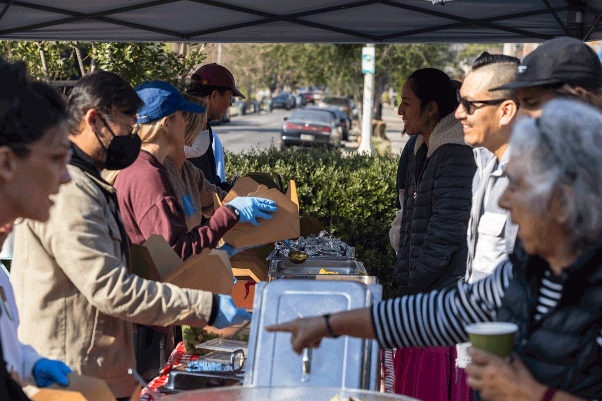World Central Kitchen volunteers and workers standing under a tent serving food to a community in Los Angeles.