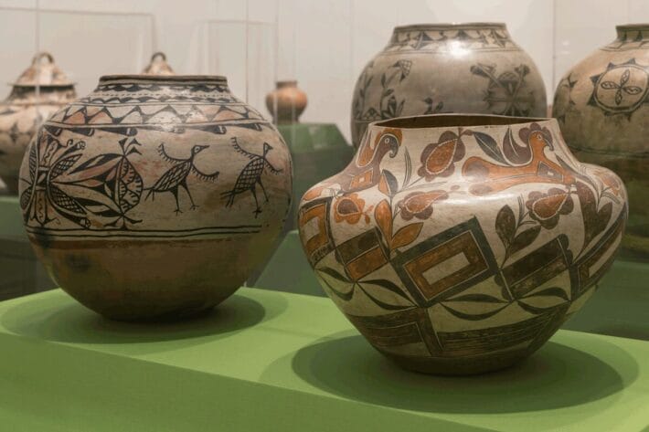 Two large patterned clay jars in a light green display case. There are various pieces of pottery visible behind them.