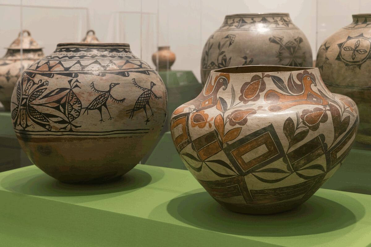 Two large patterned clay jars in a light green display case. There are various pieces of pottery visible behind them.