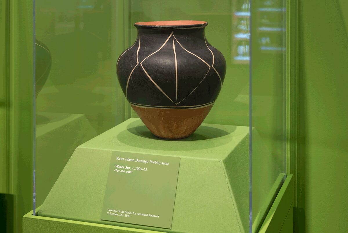 A black and red water jar with a large geometric pattern on view in a lime green display case.
