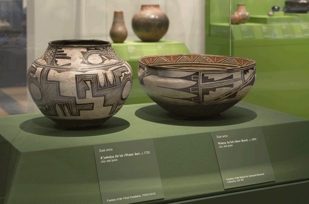 Two large pottery pieces—a water jar (left) and a stew bowl (right)—on view in a dark green display case.