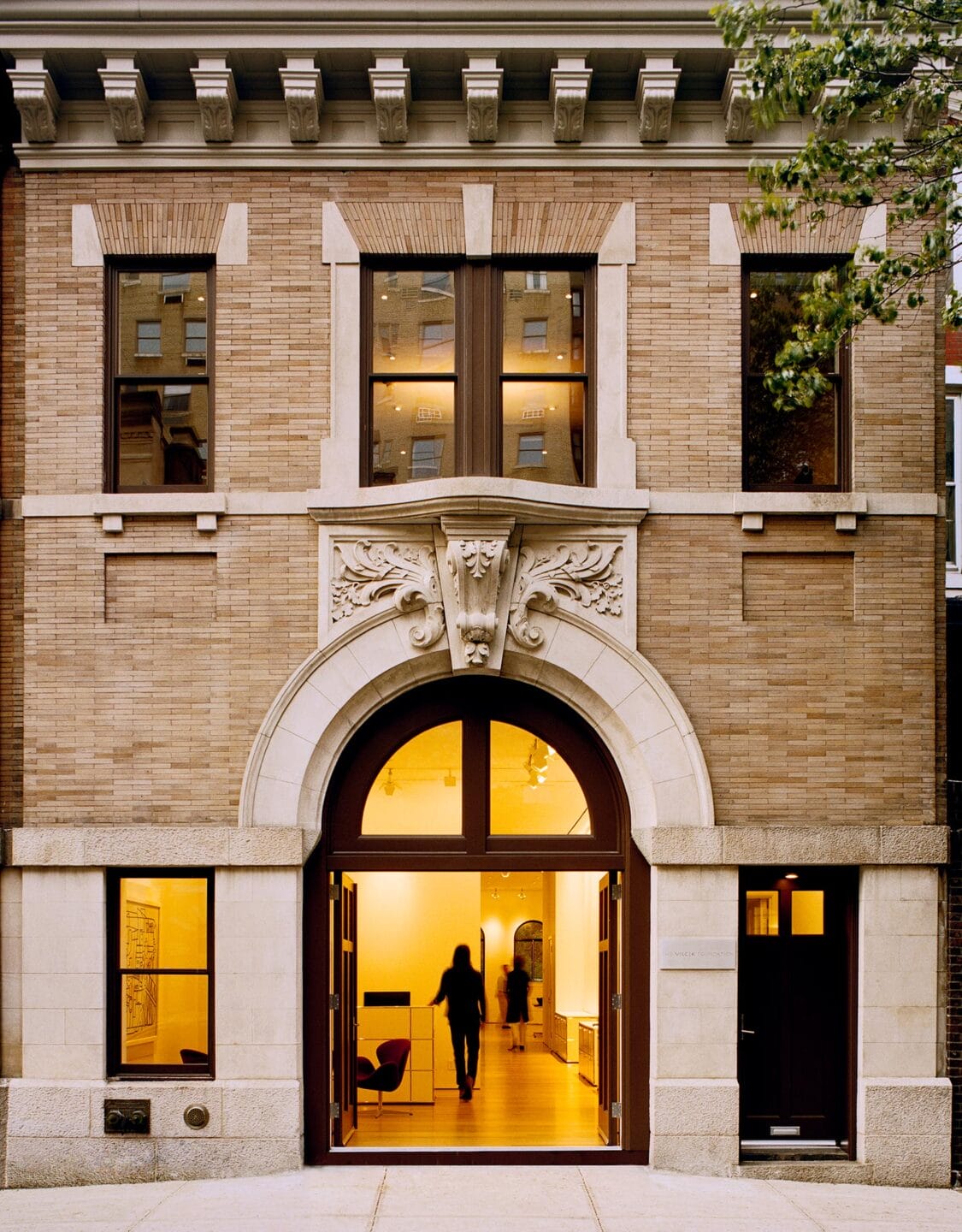 Exterior view of the Vilcek Foundation’s renovated Beaux-Arts carriage house at 167 East 73rd Street, with light glowing from its arched entrance.
