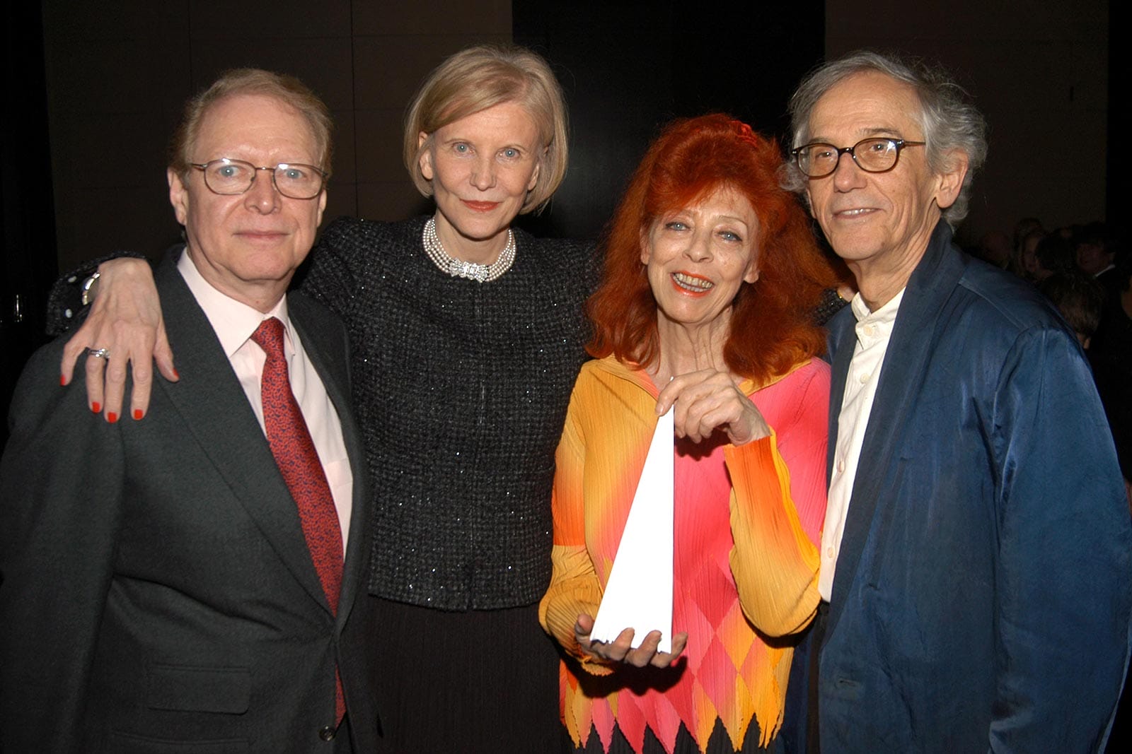 Four people pose together at an event, with one woman in a colorful outfit holding a white award.