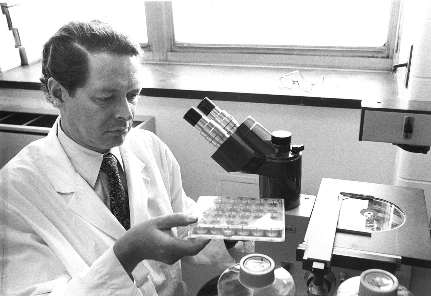 Jan Vilcek examines a lab plate beside a microscope in a research laboratory.