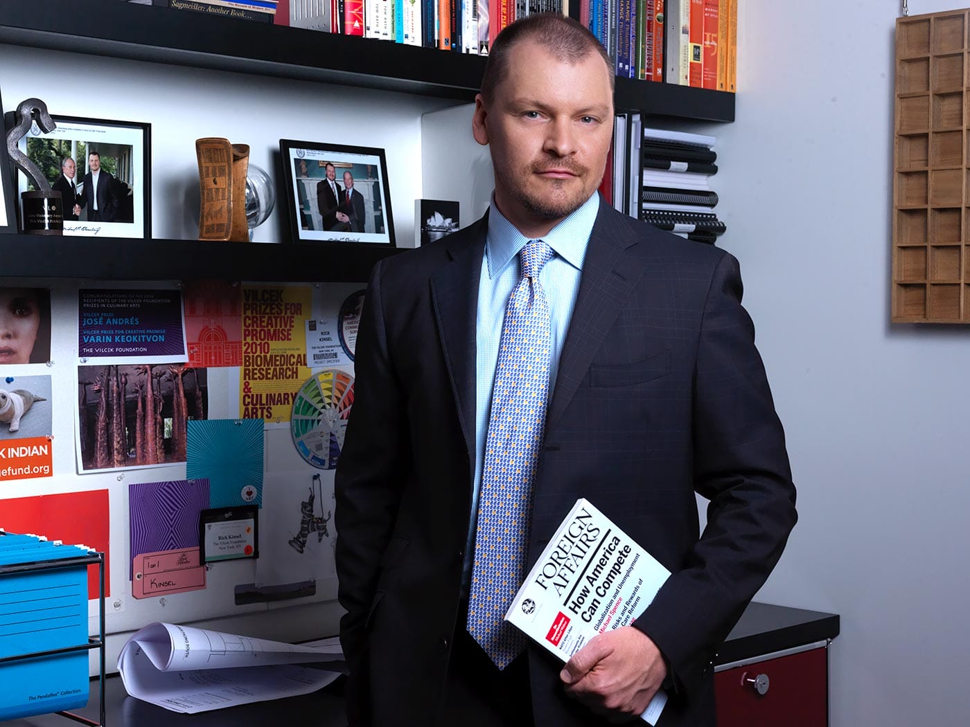 Rick Kinsel, in a suit with blue tie, holds exhibition material in an office.