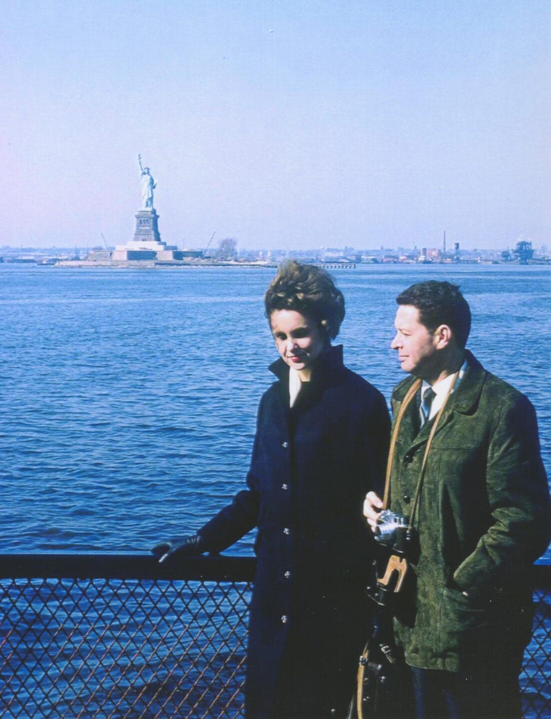 Marica and Jan Vilcek stand on a ferry with the Statue of Liberty visible across the water in the distance.