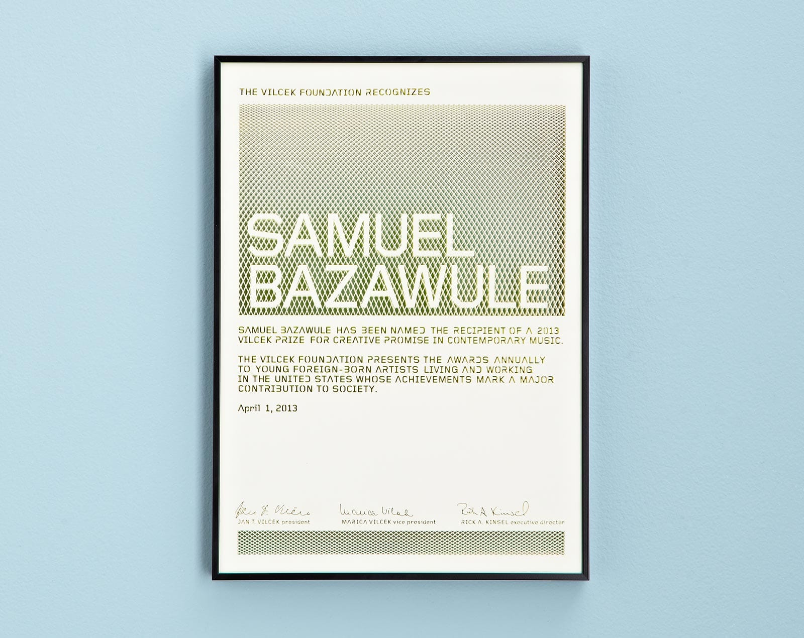 A framed Vilcek Foundation award certificate honoring Samuel Bazawule hangs on a light blue wall.