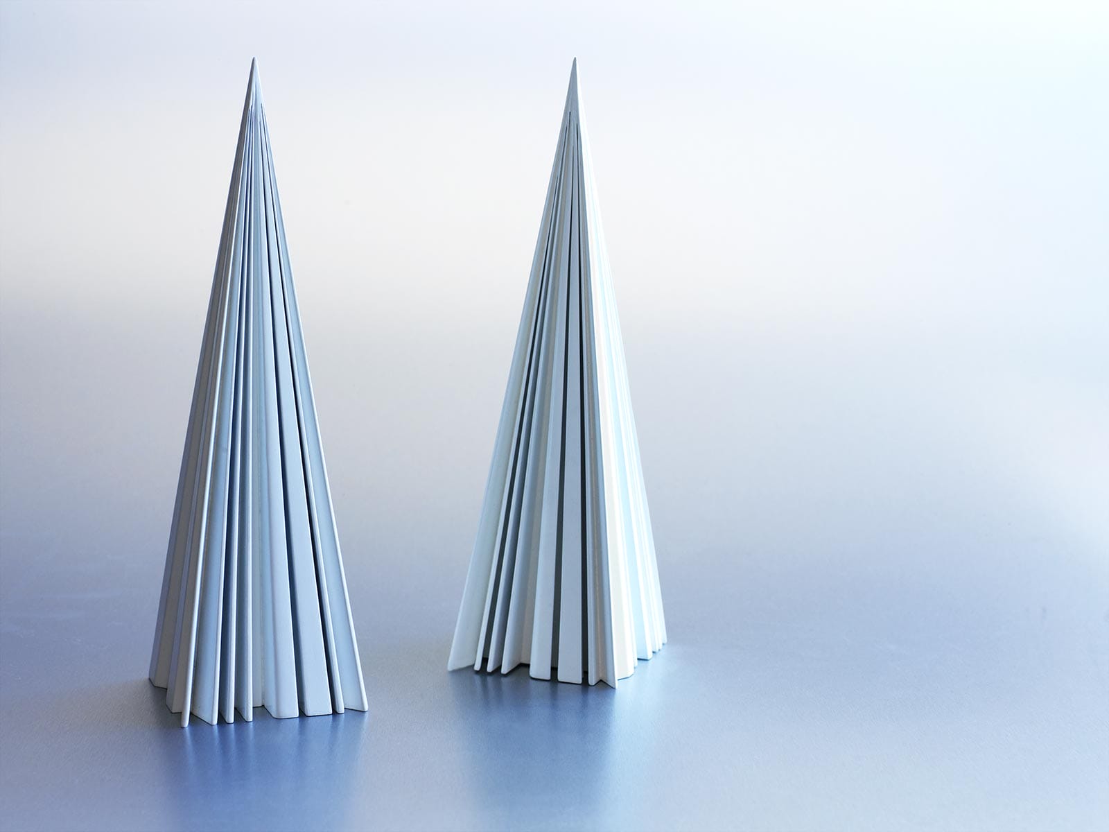 Two angular, cone-shaped Vilcek Prize sculptures stand side by side on a smooth, light-toned surface.