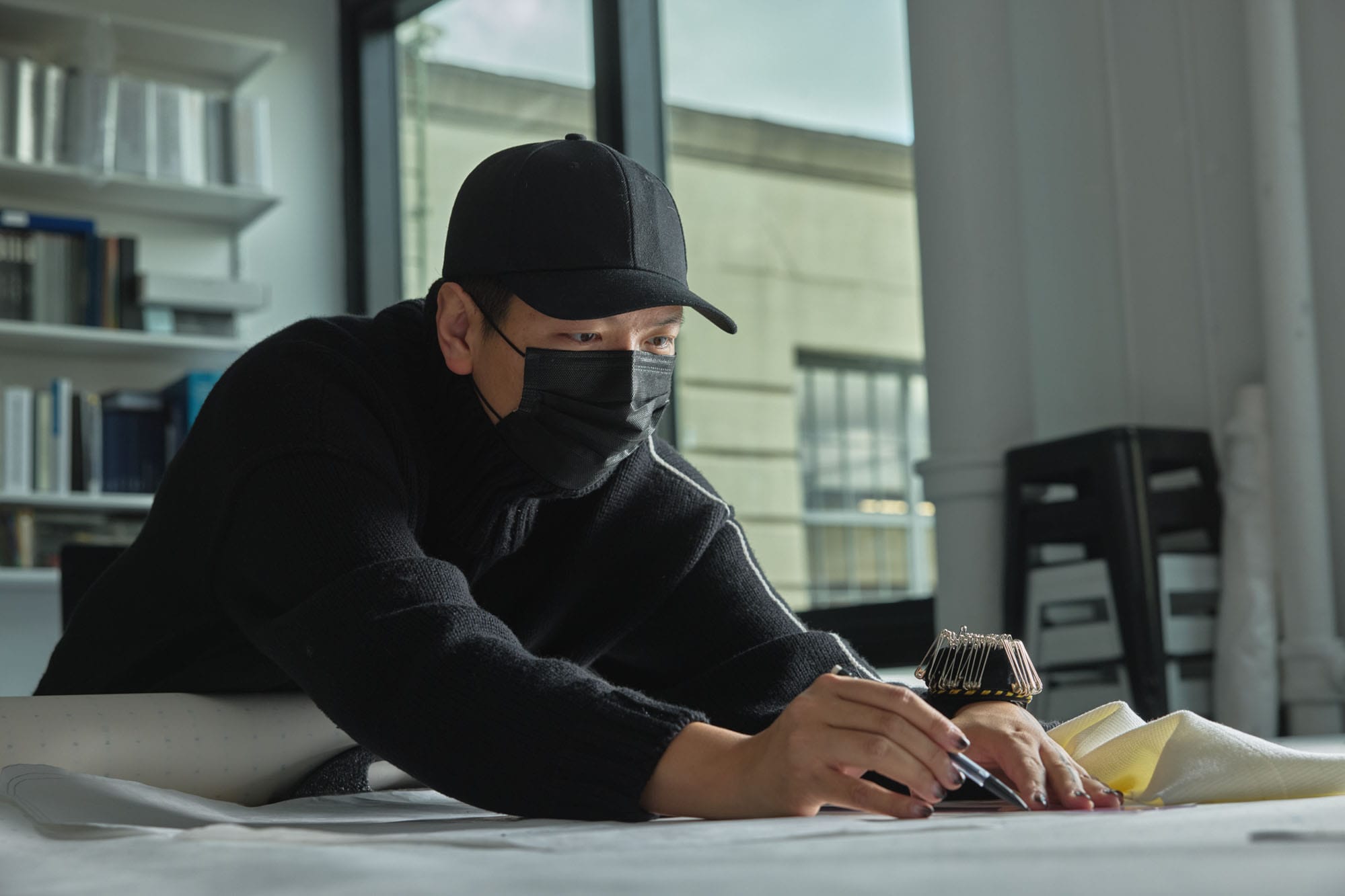 Peter Do working with a piece of clothing in his studio, surrounded by design materials.